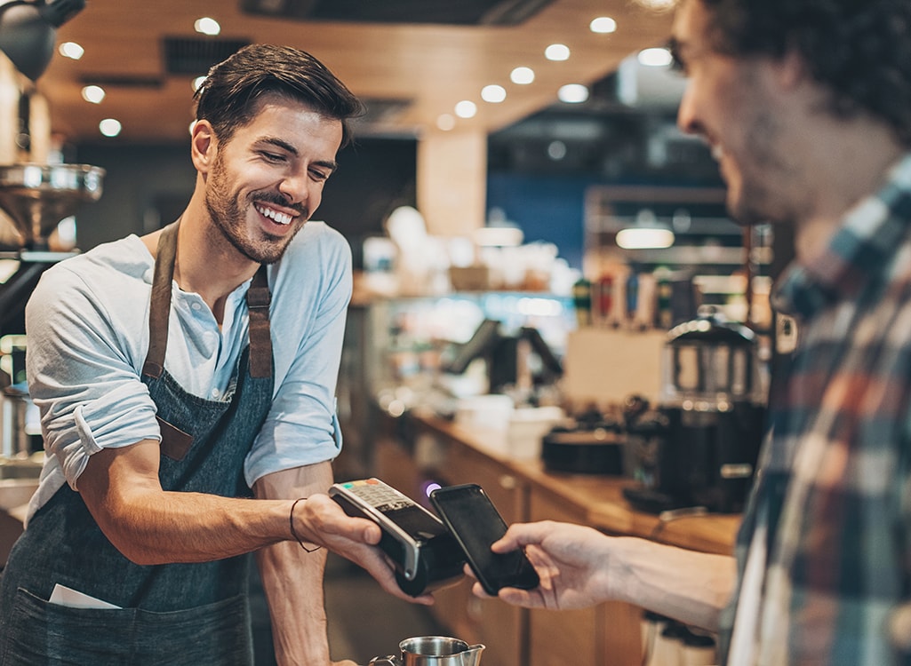 Man completes a contactless payment with his phone at coffee shop.